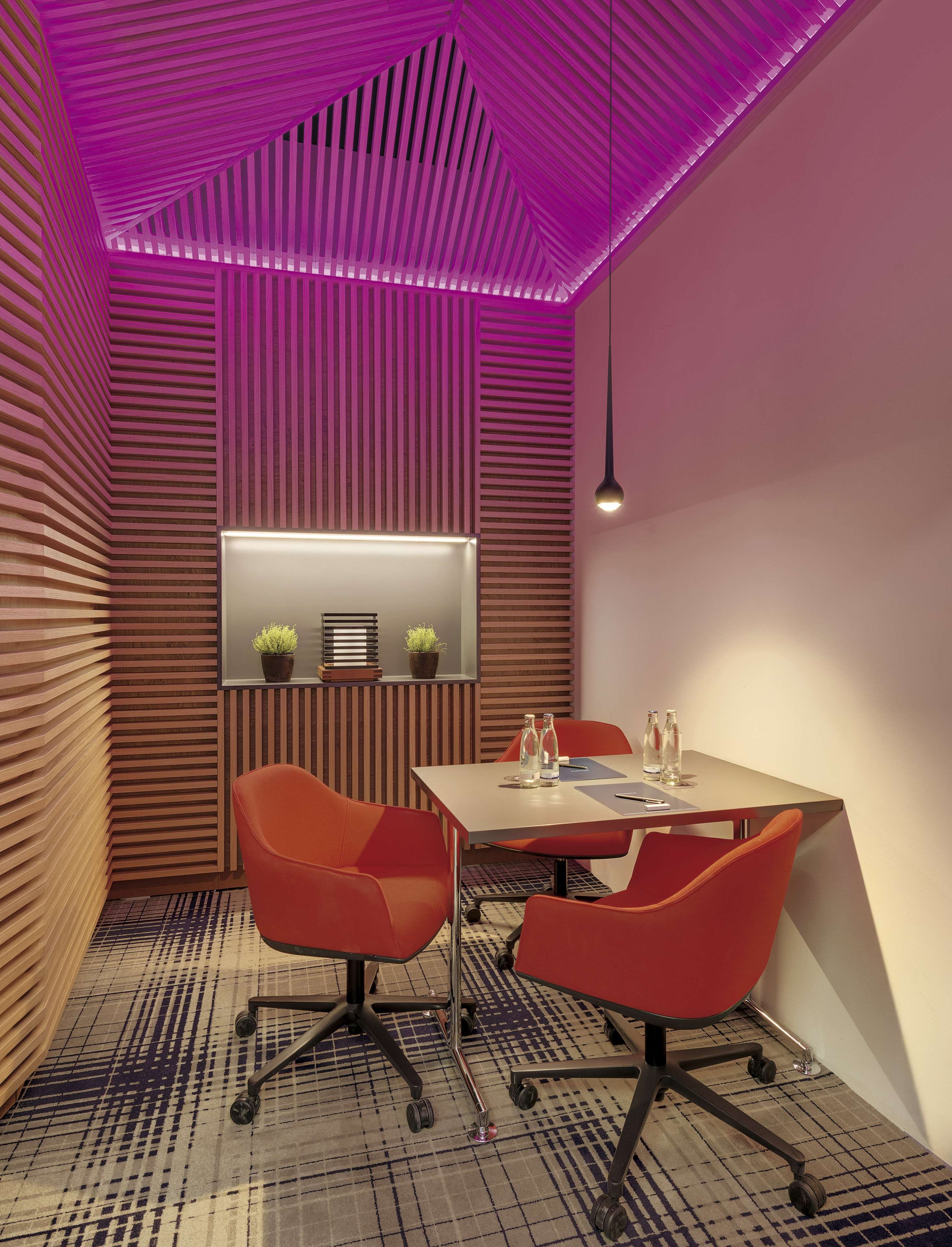 Una sala de reuniones moderna con una mesa, sillas y un techo inclinado con iluminación morada.