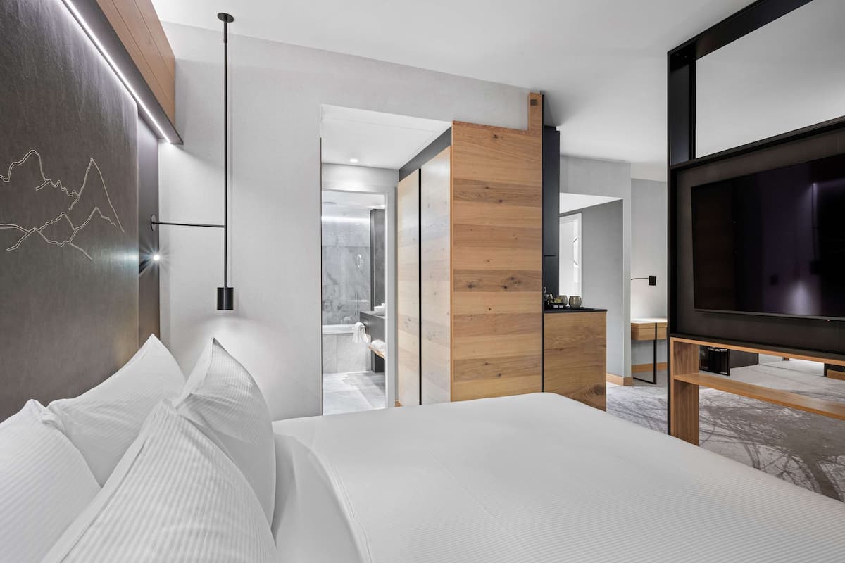 A modern hotel room with a large bed, a TV, and a wooden wardrobe.