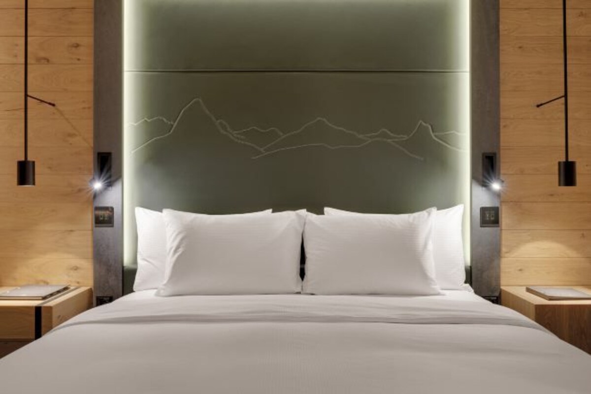 Habitación de hotel moderna con una cama grande, cabecero de madera e iluminación colgante.