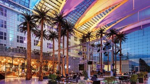 A spacious indoor atrium with high ceilings, palm trees, and modern seating areas.