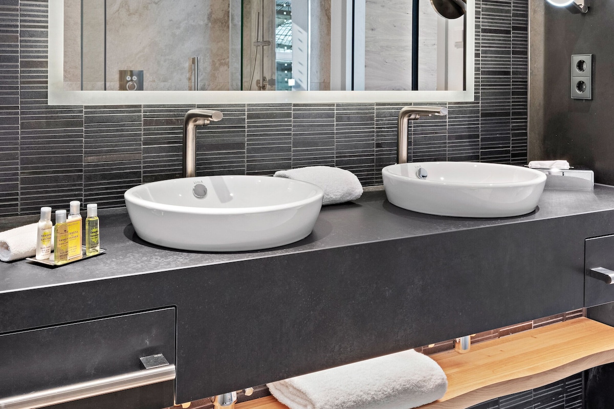 A modern bathroom with two sinks, a large mirror, and a wooden bench.