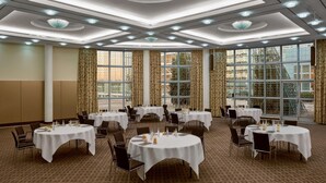 A conference room with multiple tables, chairs, and a large window with curtains.