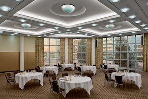A conference room with multiple tables, chairs, and a large window with curtains.