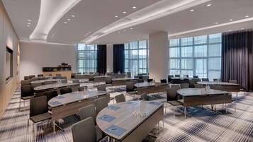 Un salón de conferencias con varias mesas y sillas, ventanas amplias y un diseño moderno del techo.