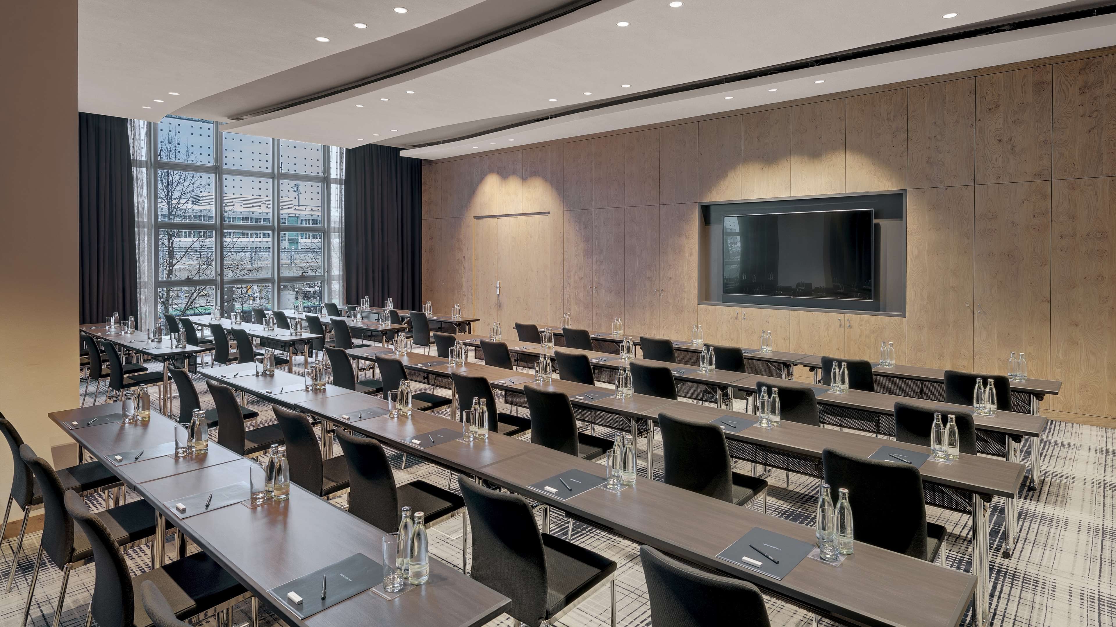A conference room with long tables, chairs, and a large screen on the wall.