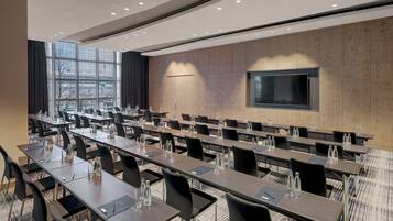A conference room with long tables, chairs, and a large screen on the wall.