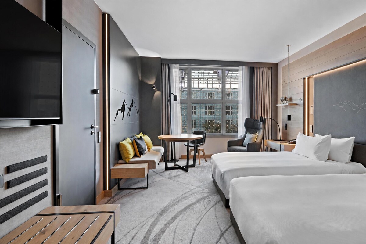 Habitación de hotel con televisión, dos camas, un sofá, una mesita y vistas a la ciudad.