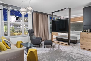Una sala de estar moderna con sofá, sillón, puf y televisor sobre un mueble de madera.