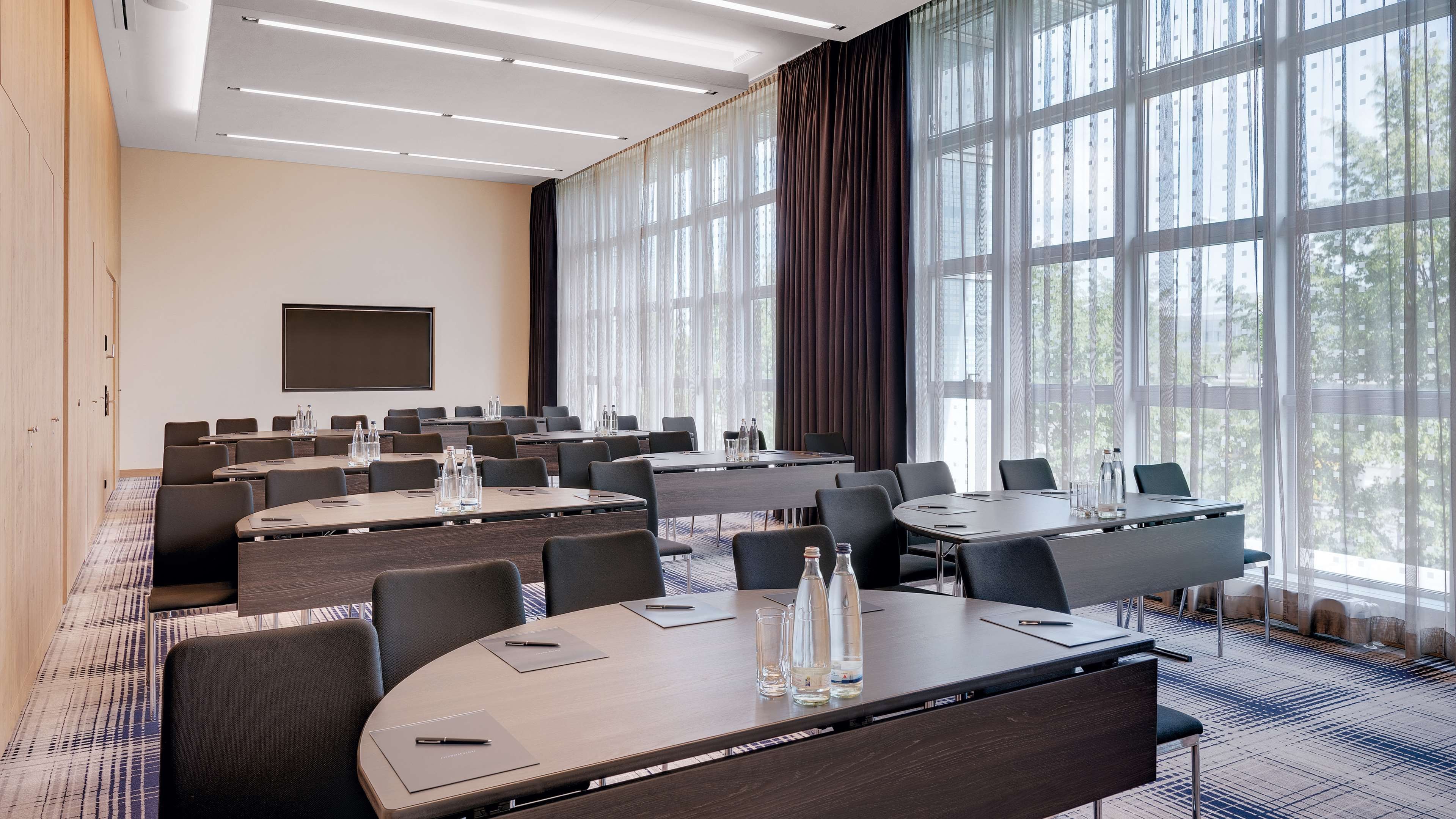 A conference room with multiple tables, chairs, and a large window with curtains.