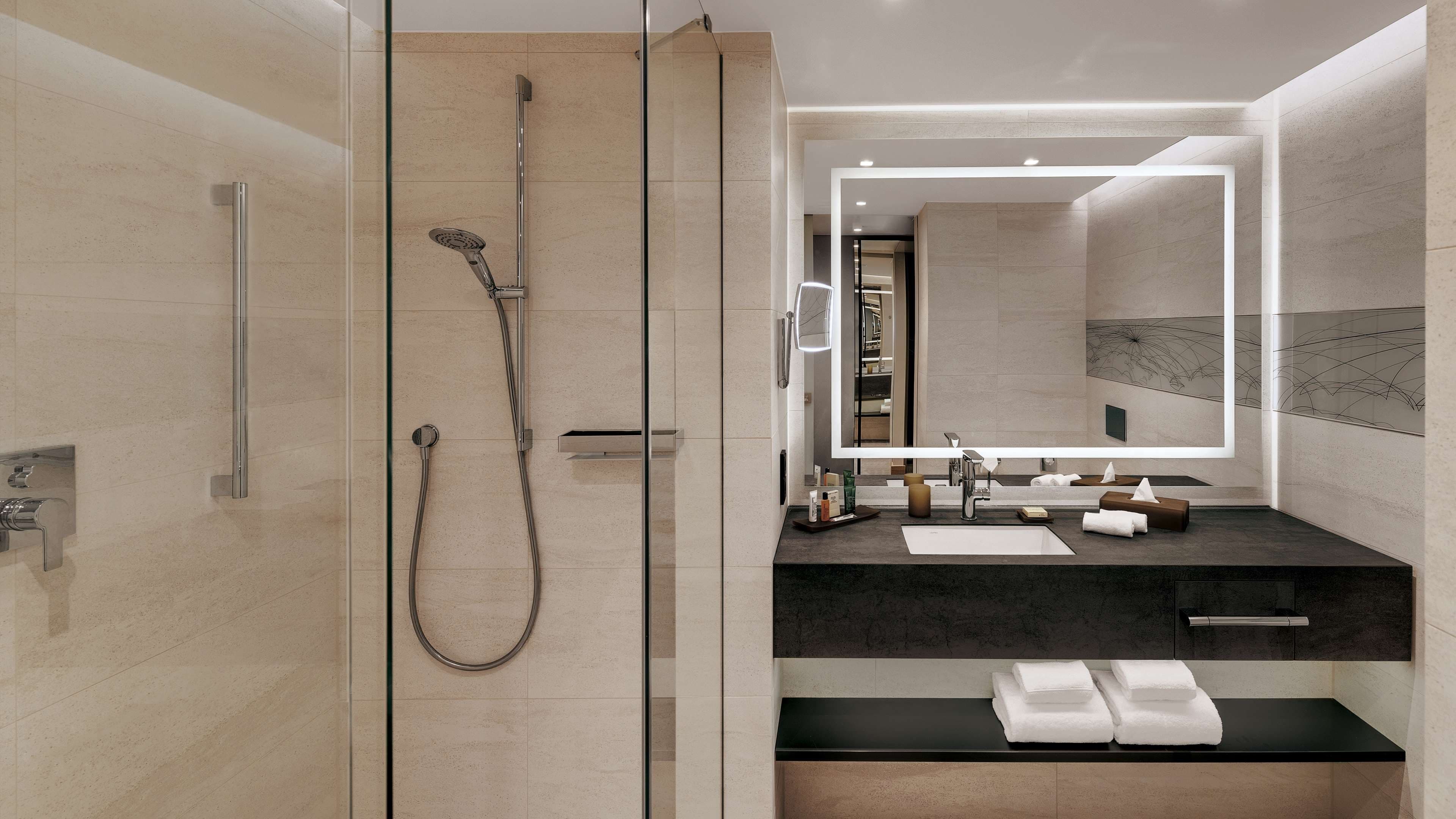 A modern bathroom with a glass-enclosed shower, a large mirror, and a vanity with a black countertop.