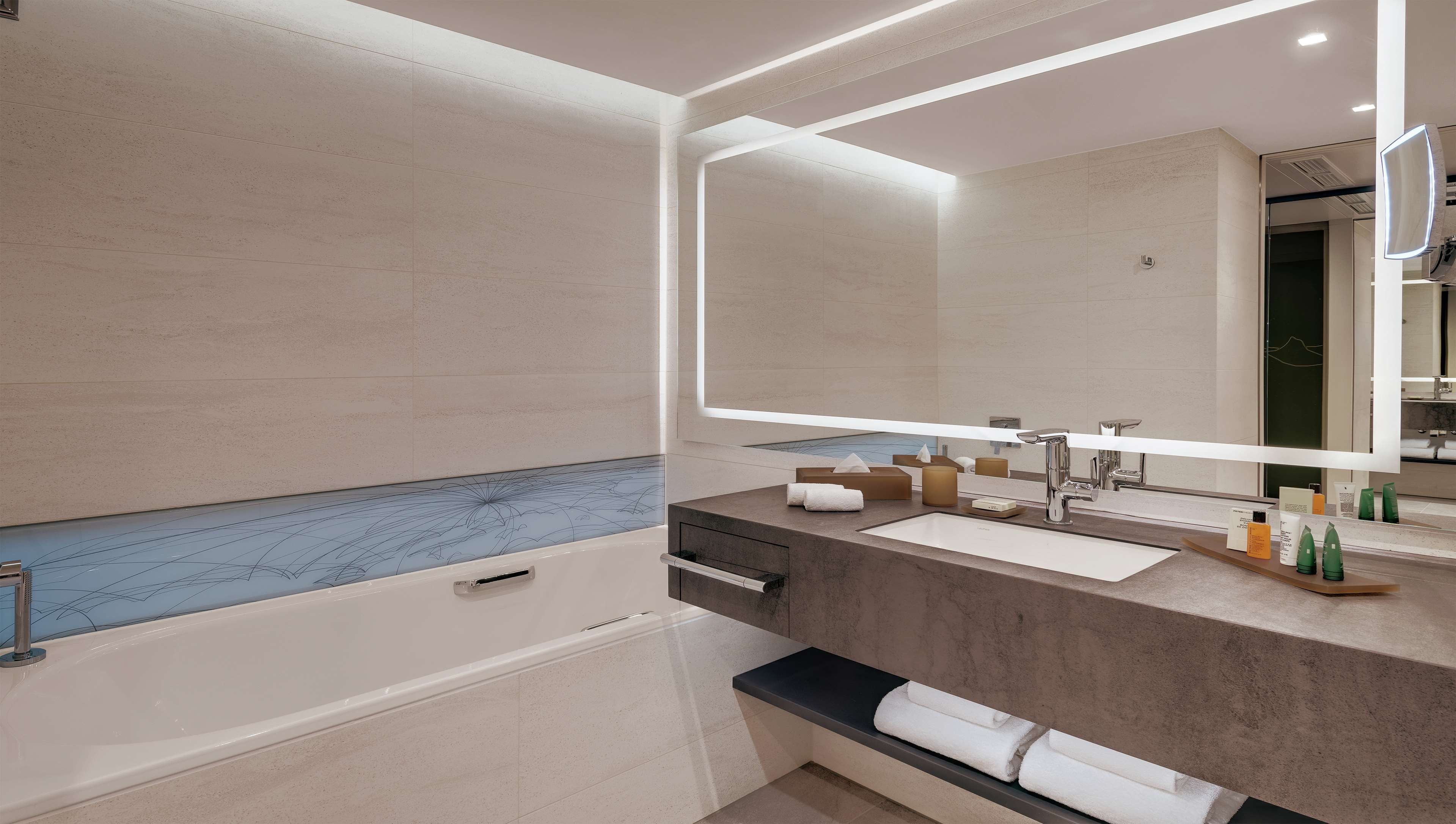 A modern bathroom with a large mirror, a bathtub, and a vanity with toiletries.