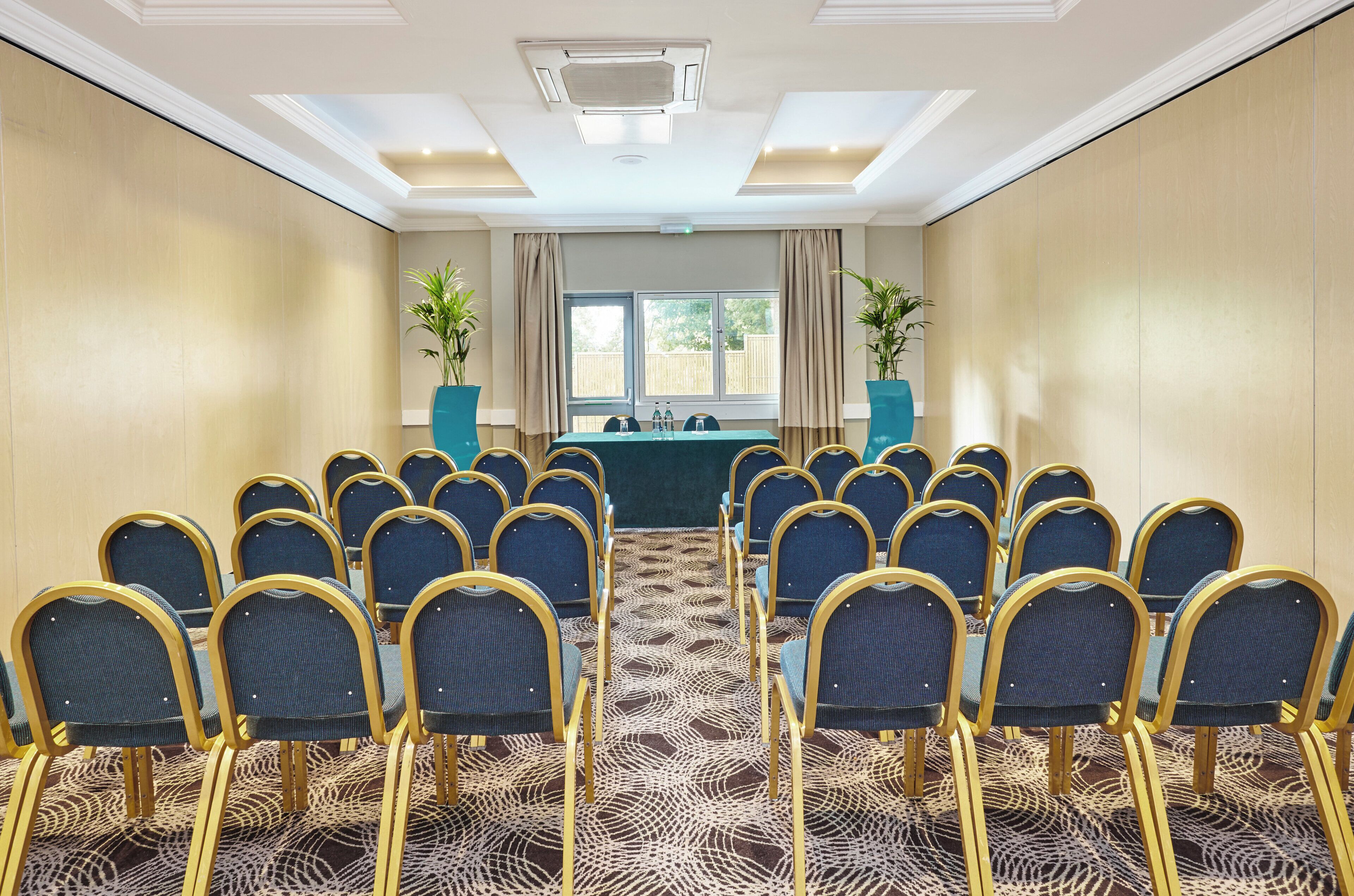 A conference room with rows of chairs, a table with water bottles, and two potted plants.