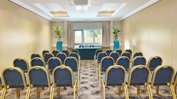 A conference room with rows of chairs, a table with water bottles, and two potted plants.