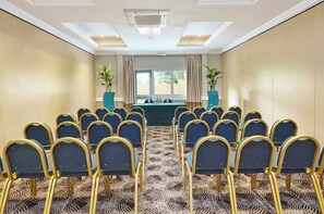 A conference room with rows of chairs, a table with water bottles, and two potted plants. - Holiday Inn Cardiff - North M4 by IHG (Cardiff)