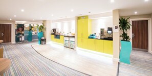 Un moderno vestíbulo de hotel con una recepción, una zona de estar y una kitchenette.