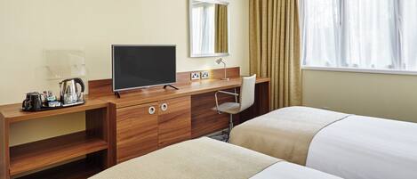 Een hotelkamer met een houten bureau, een flatscreen televisie, een koffiezetapparaat, twee bedden, een stoel en een raam met gordijnen.