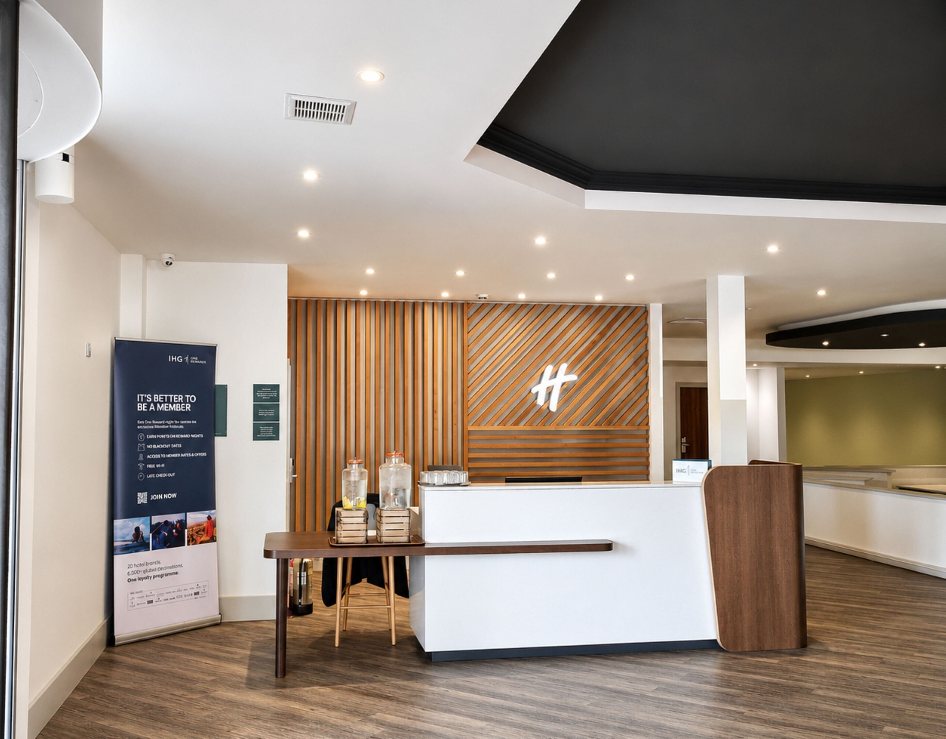A modern hotel reception area with a wooden reception desk, a large signboard, and a wall-mounted logo.