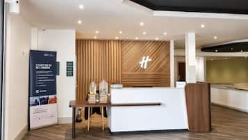 A modern hotel reception area with a wooden reception desk, a large signboard, and a wall-mounted logo.