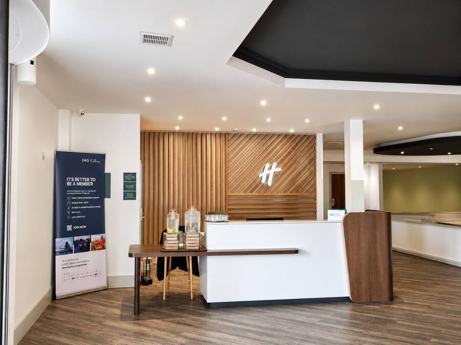Una moderna zona de recepción de hotel con un mostrador de madera, un gran cartel y un logotipo montado en la pared.