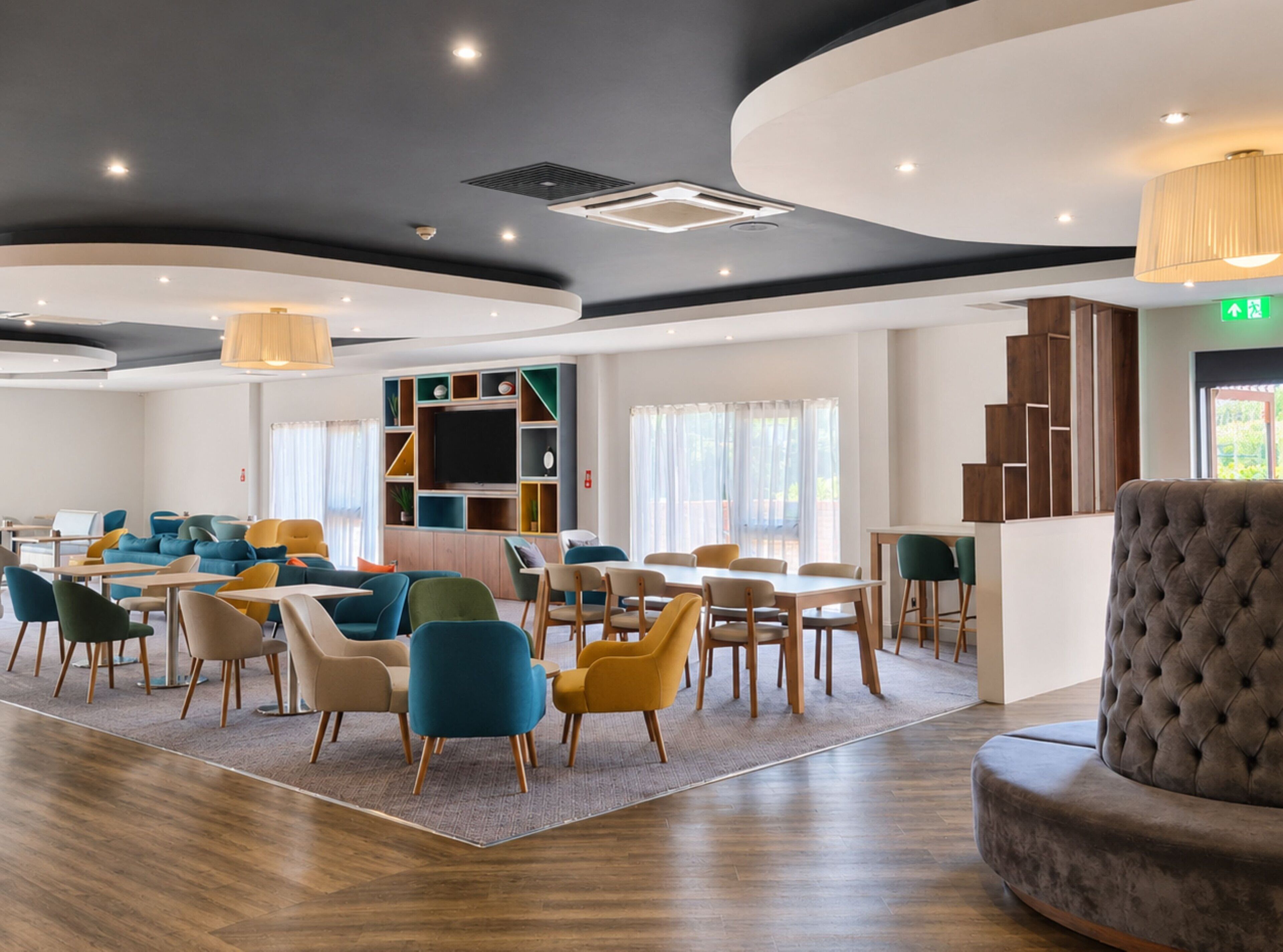 Eine moderne Hotelhalle mit gewölbter Decke, einer Sitzecke mit bunten Stühlen, einem Flachbildfernseher und einer Treppe.