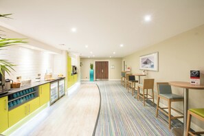 A hotel lobby with a kitchen area, seating area, and a door leading to another room. - Holiday Inn Cardiff - North M4 by IHG (Cardiff)