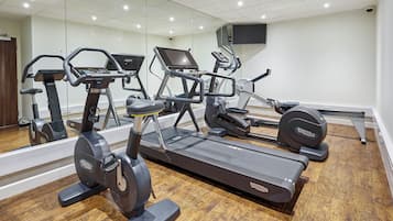 Ein Fitnessstudio mit mehreren Trainingsgeräten, einem Holzboden und einem großen Spiegel, der den Raum widerspiegelt.