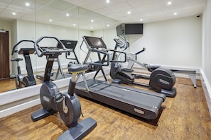 A gym with multiple exercise machines, a wooden floor, and a large mirror reflecting the space. - Holiday Inn Cardiff - North M4 by IHG (Cardiff)