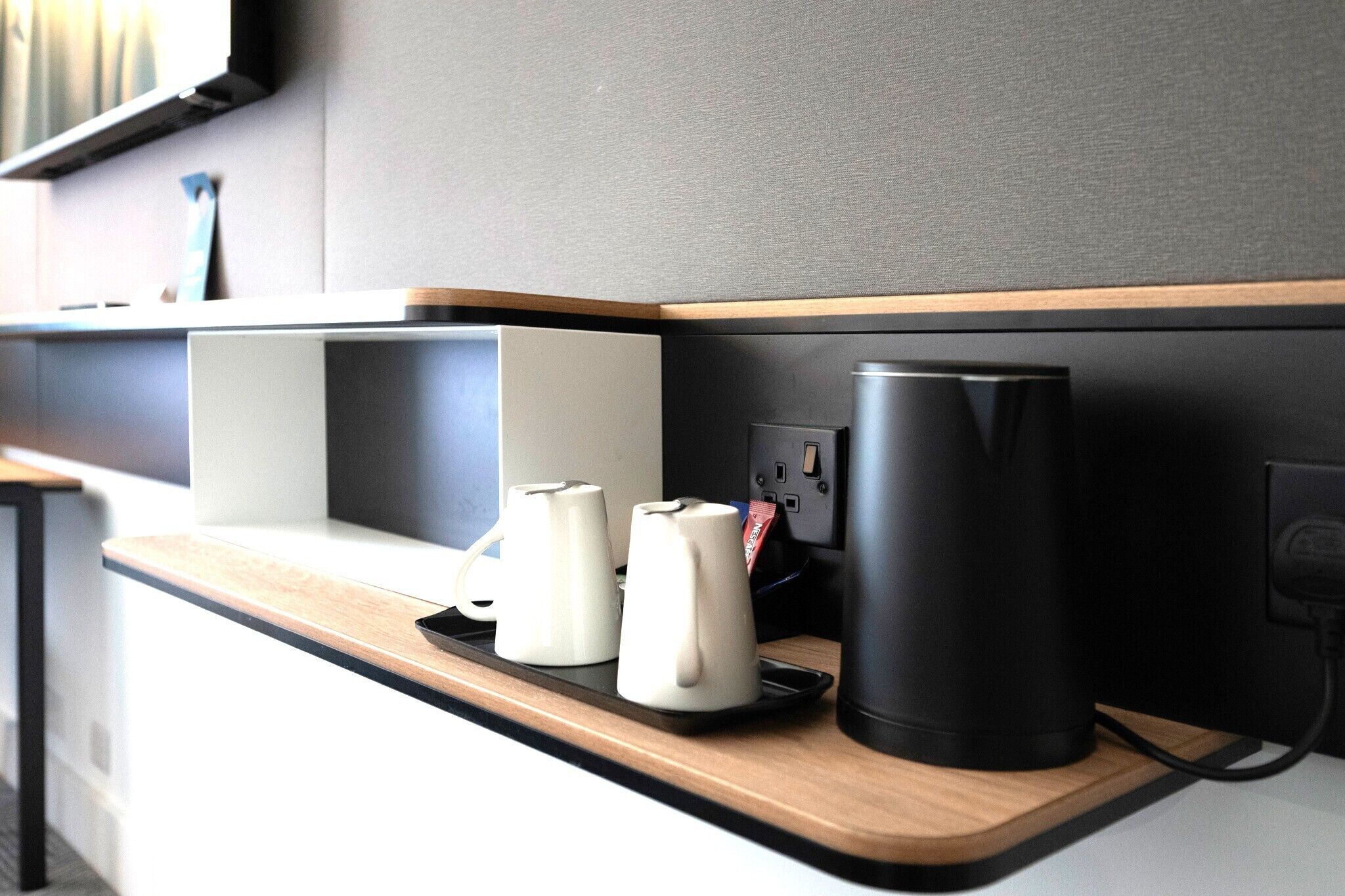 Una cocina moderna con estación de carga integrada, una cafetera y un electrodoméstico cilíndrico negro sobre una encimera de madera.