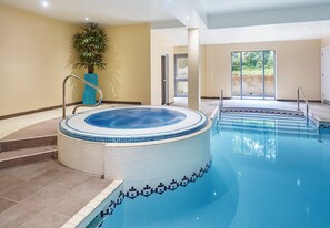 A large indoor swimming pool with a hot tub, surrounded by beige walls and a potted plant.