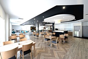 A modern dining area with wooden tables and chairs, a kitchen area with a counter, and a herringbone floor pattern.