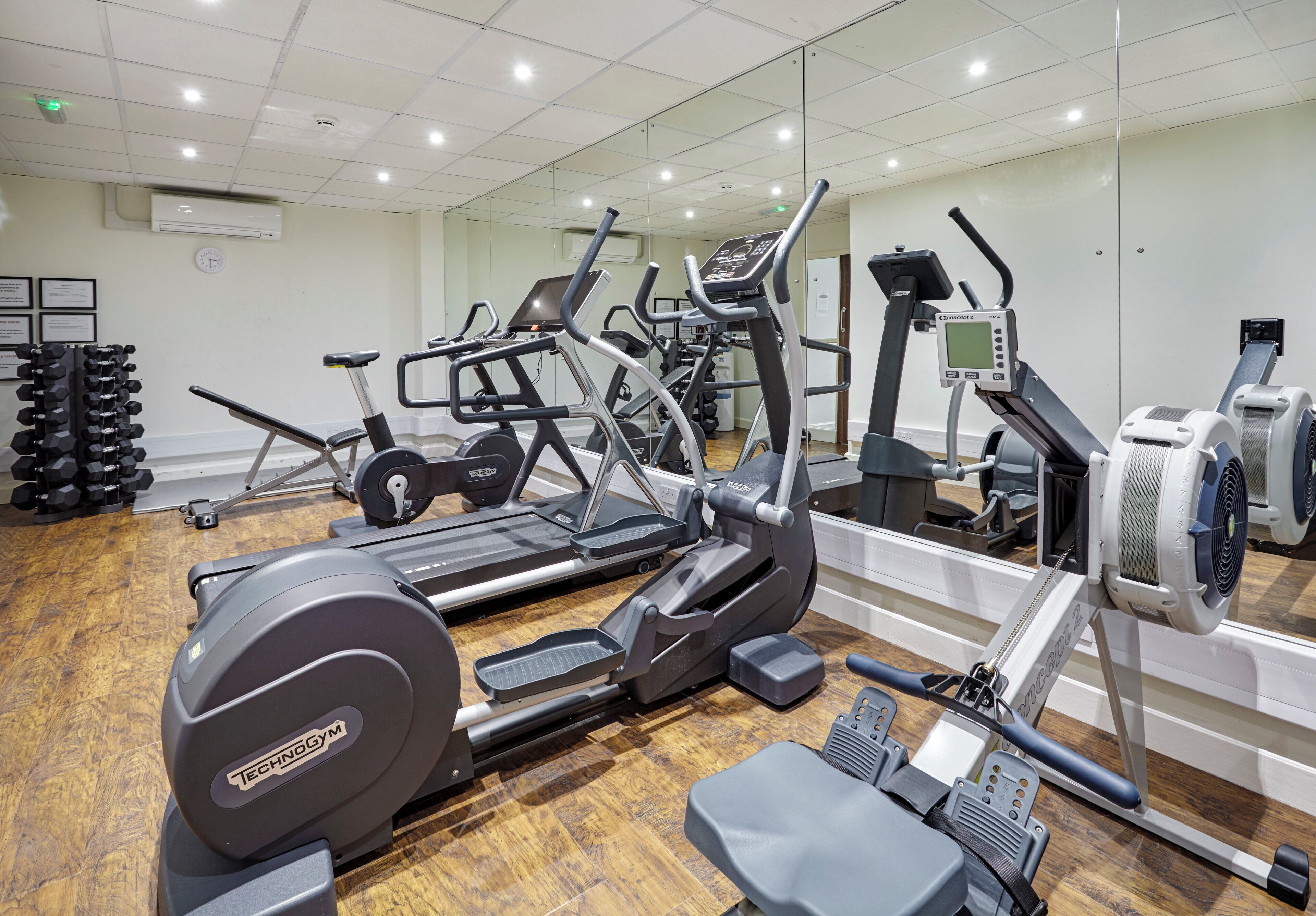 Un gimnasio con equipo de ejercicio diverso, incluyendo cintas de correr, elípticas y bancos de pesas.