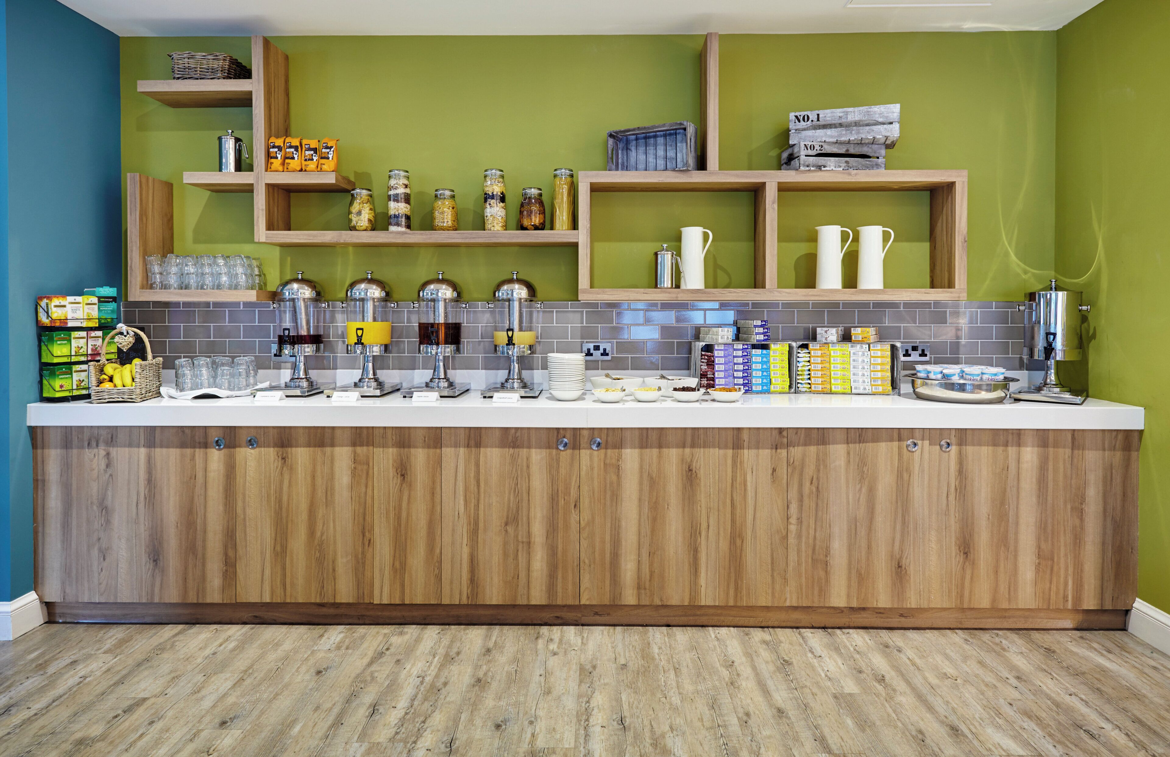 A kitchen area with a wooden counter, various food items, and kitchen appliances.