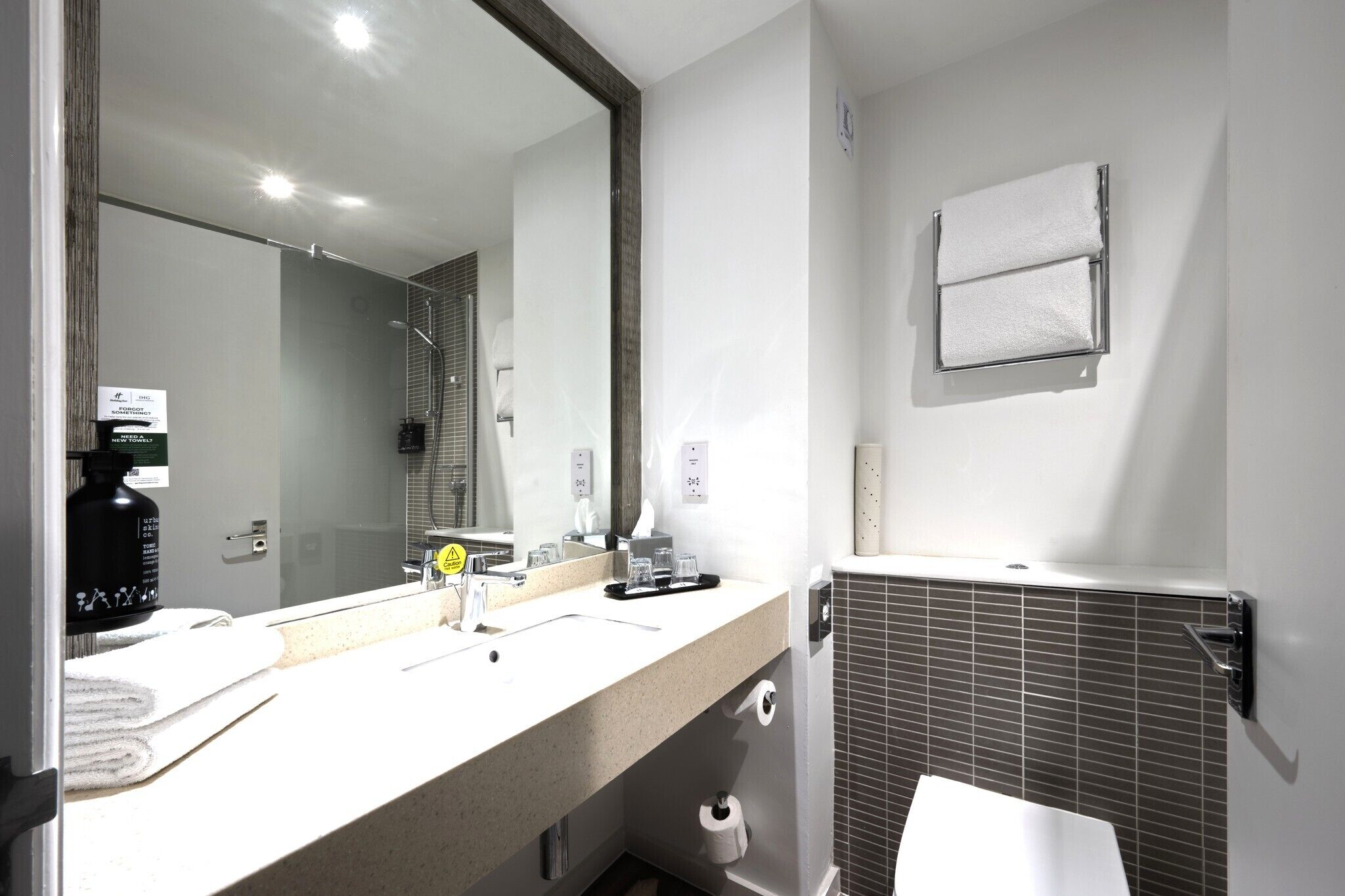 A modern bathroom with a large mirror, a sink with a towel, and a toilet.