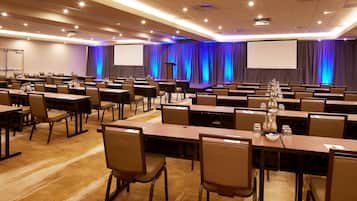 Un salón de conferencias con varias mesas y sillas, un atril y una pantalla grande.