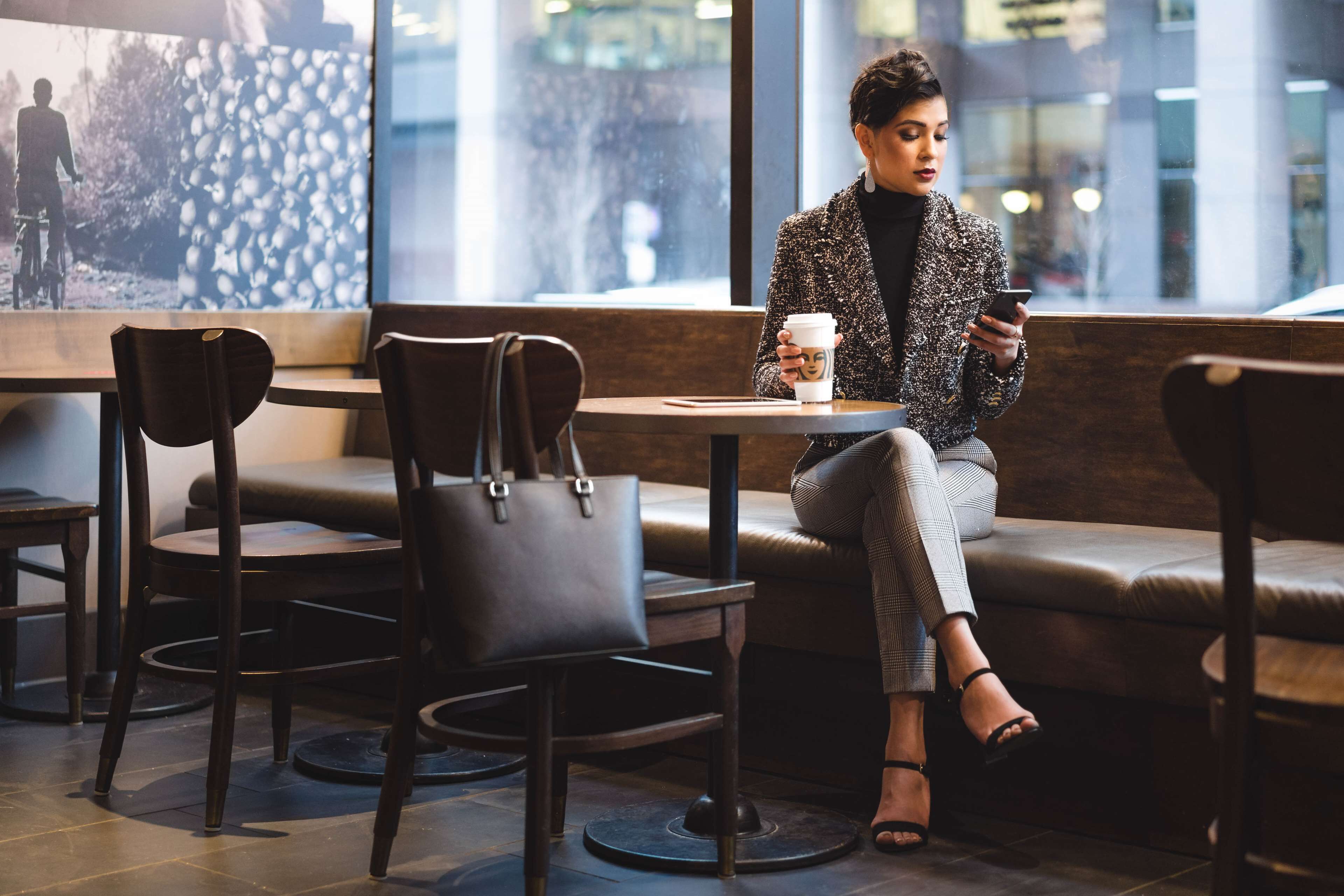 Una persona sentada a una mesa con una taza de café, en una cafetería moderna con asientos de cuero y un amplio ventanal.