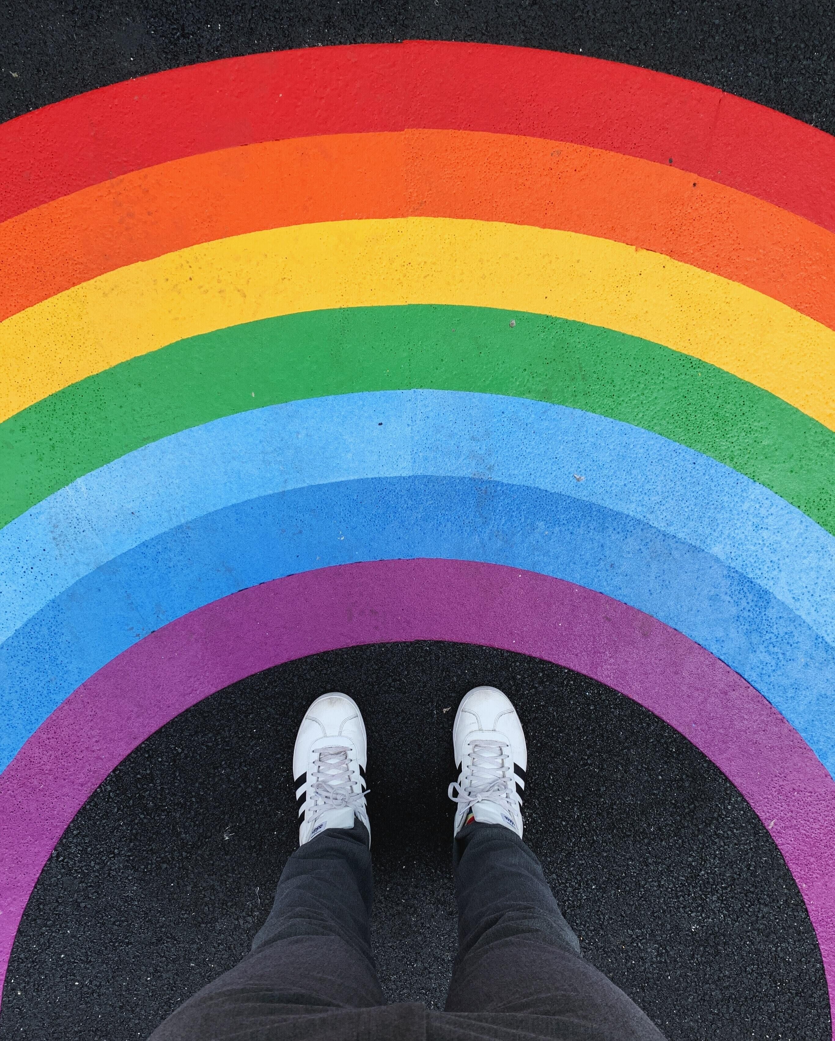 A person standing on a rainbow-colored pavement with white sneakers.