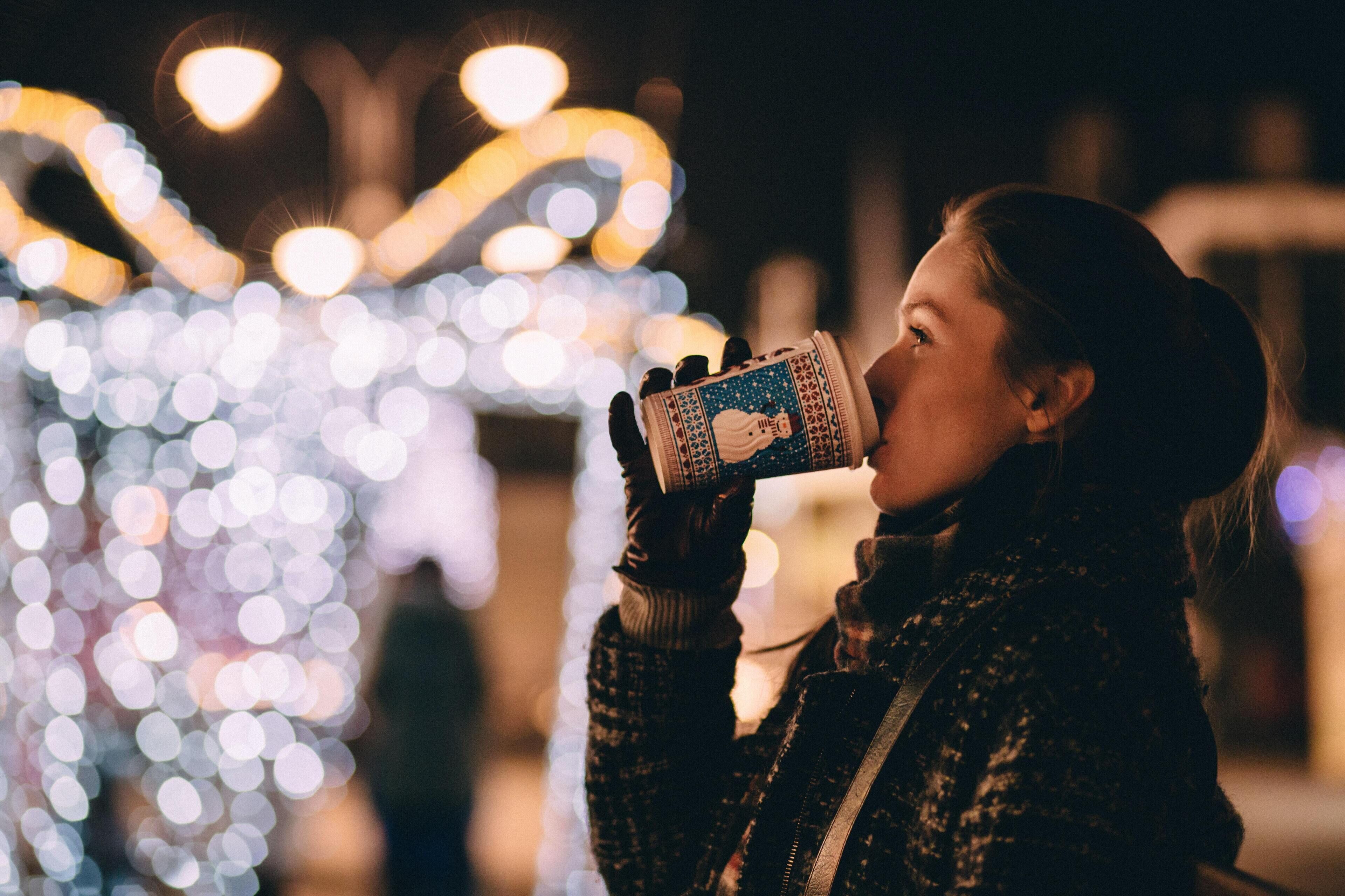 A person holding a cup, with a blurred background of lights.