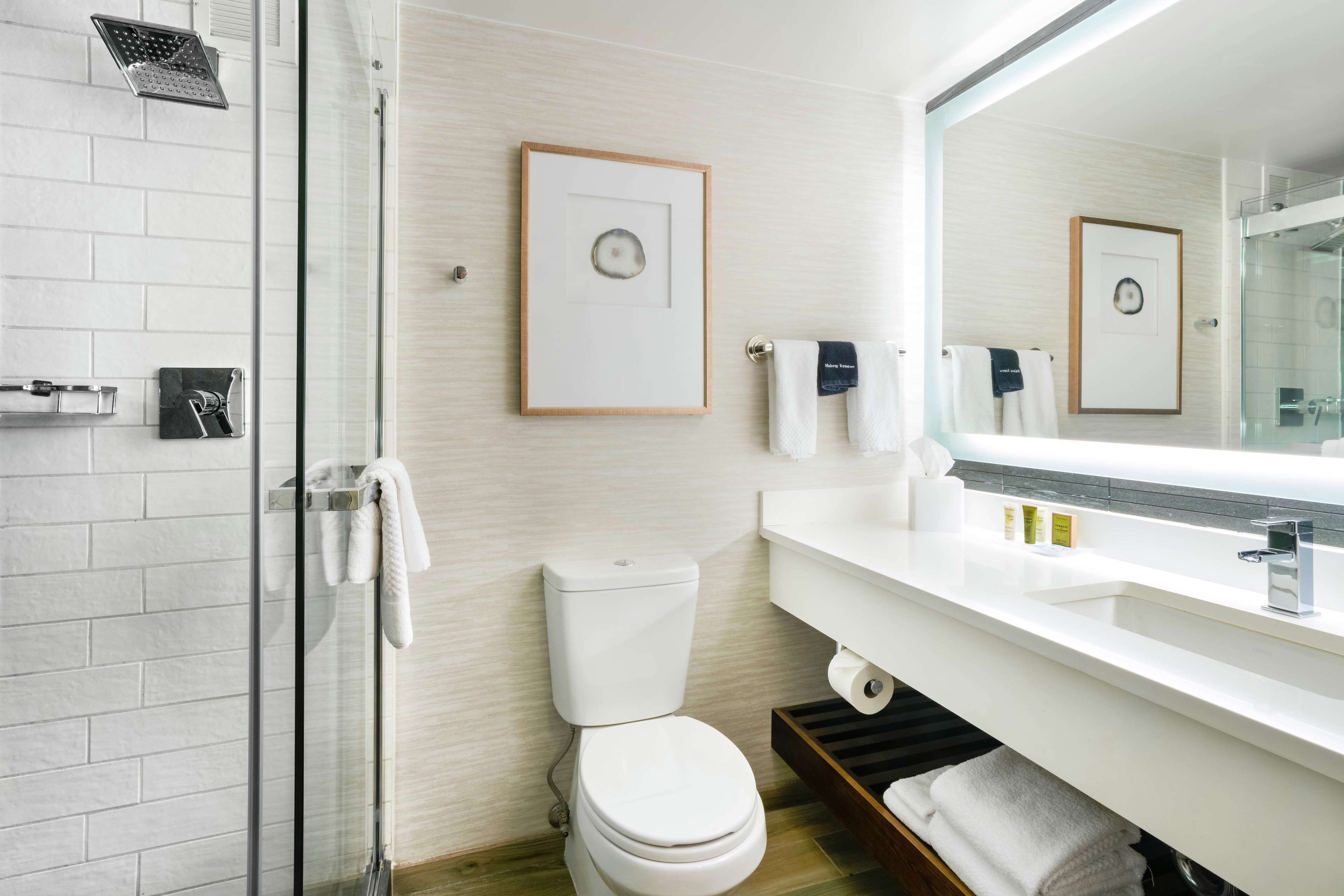 A modern bathroom with a glass shower enclosure, a white toilet, a sink with a mirror, and framed pictures on the wall.