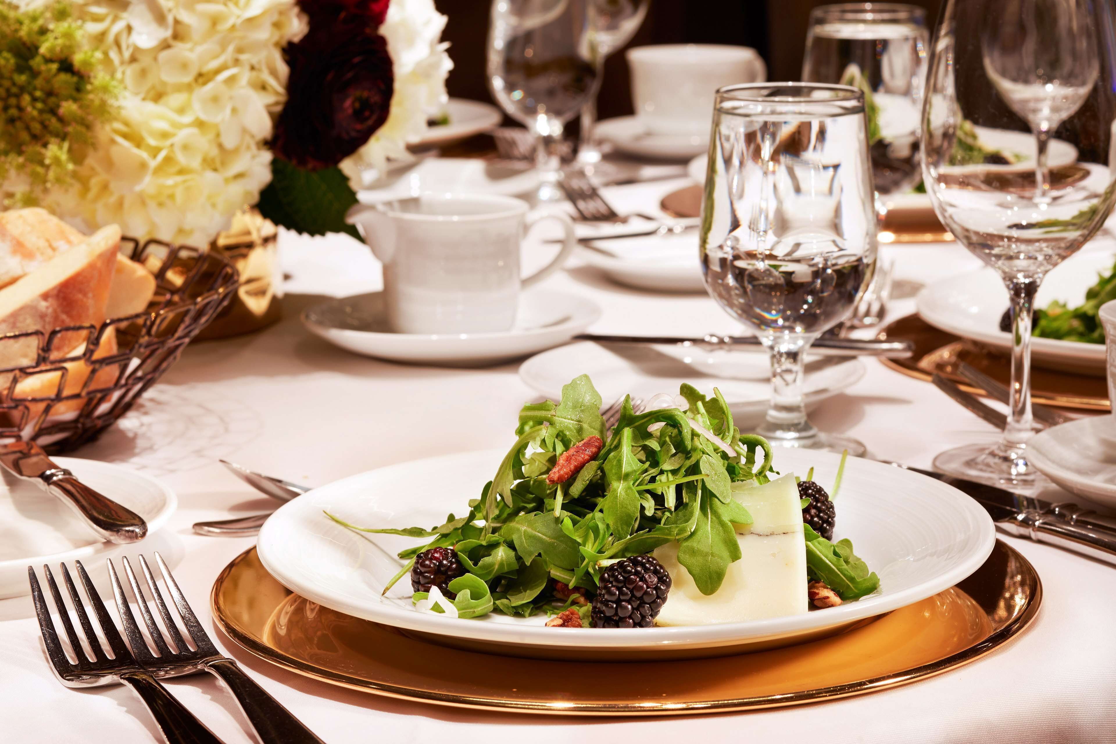 A formal dining table with a white tablecloth, a plate of salad, and various cutlery.