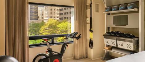 A hotel room with a stationary bike, exercise balls, and a weightlifting station.