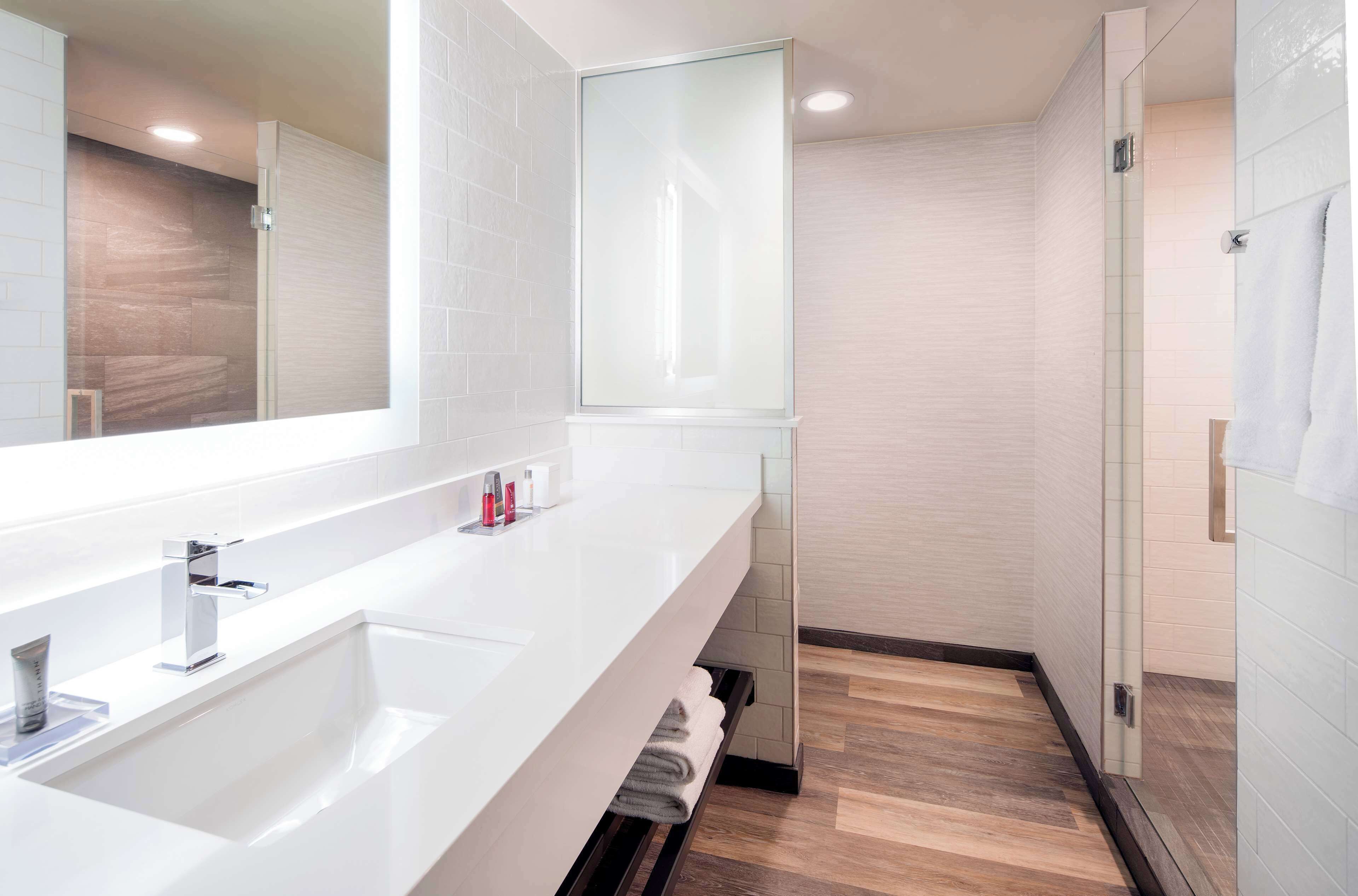 Un baño moderno con un espejo grande, un lavabo blanco y una cabina de ducha de vidrio.