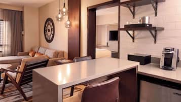 A modern hotel room with a dining area, a sofa, a coffee machine, and a TV mounted on the wall.