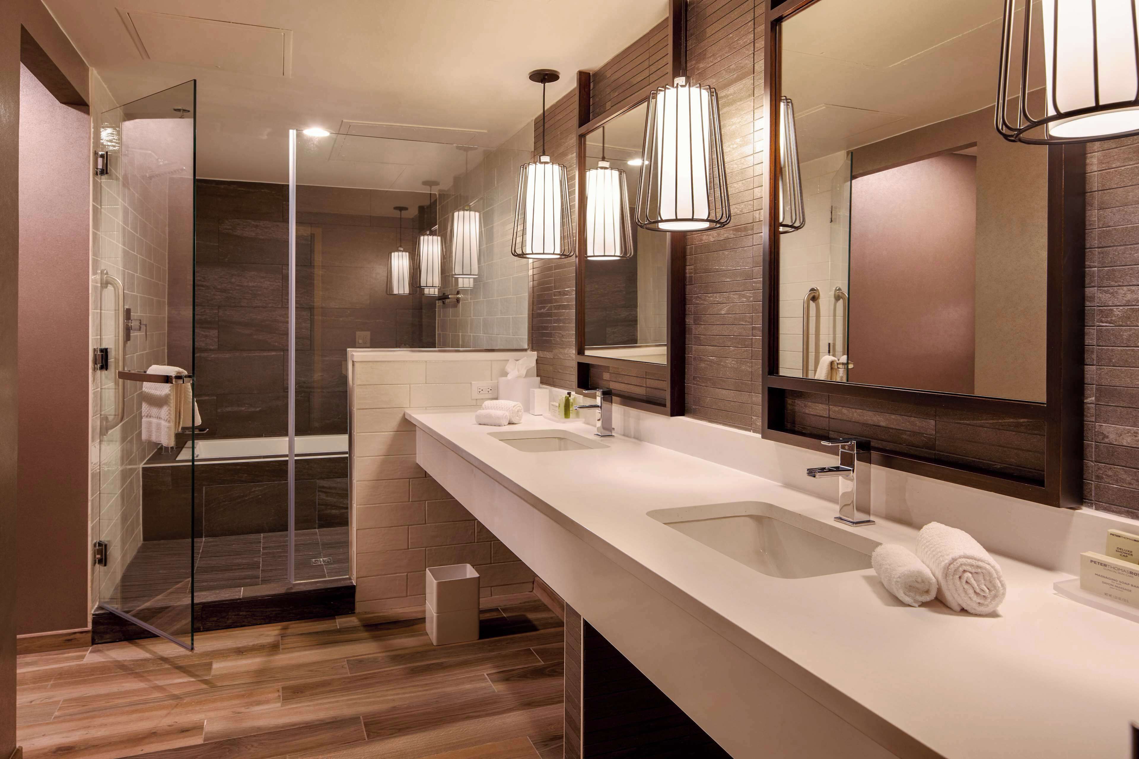A modern bathroom with a glass-enclosed shower, two sinks, and large mirrors.