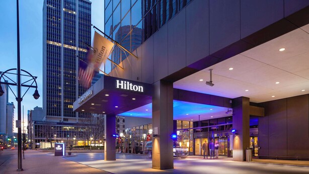 Entrada de um hotel Hilton, com fachada de vidro, letreiros iluminados e design arquitetônico moderno.