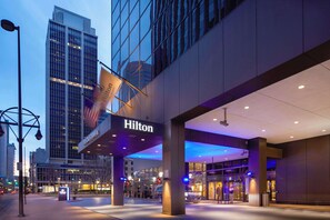 A Hilton hotel entrance with a glass facade, illuminated signage, and a modern architectural design.
