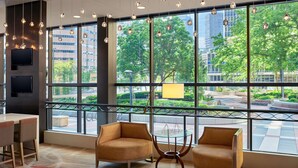 Um saguão de hotel moderno com grandes janelas, luminárias pendentes e assentos confortáveis.