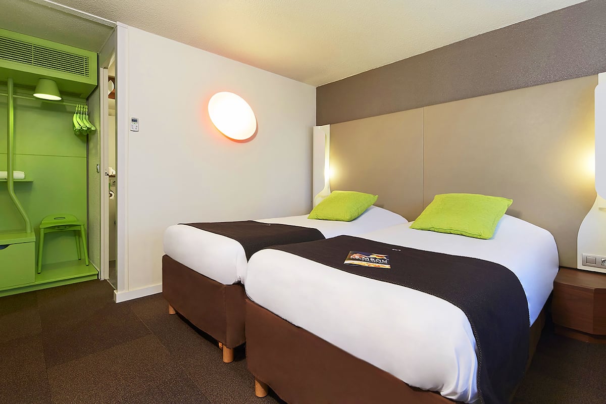A hotel room with two beds, a green bathroom, and a nightstand with a lamp.