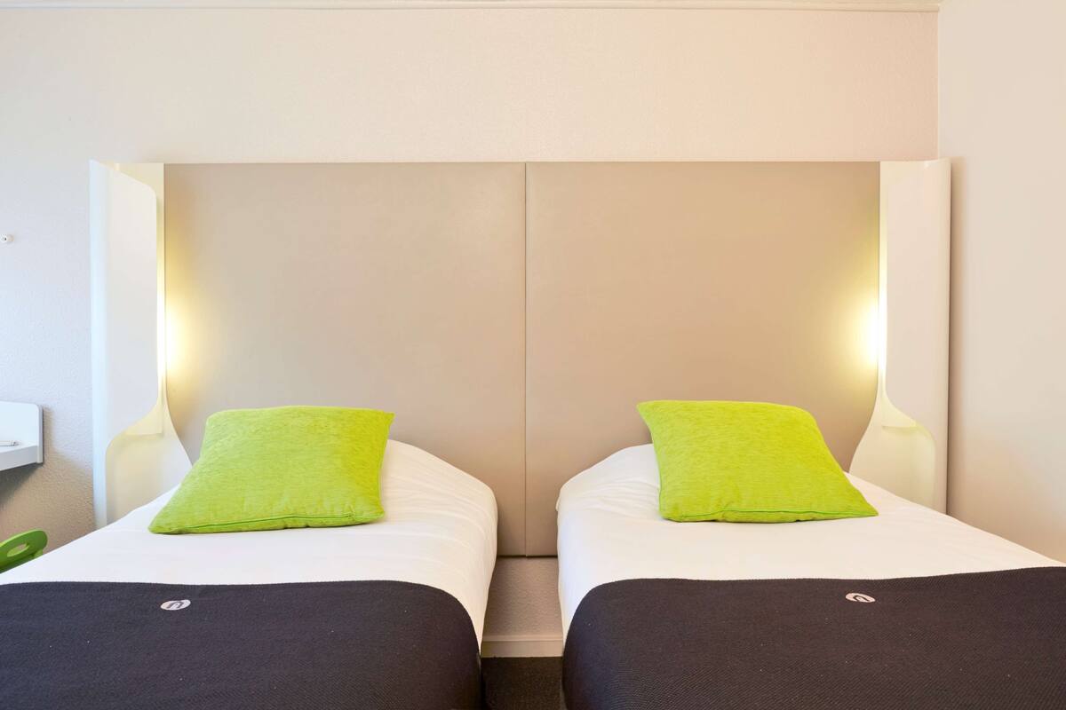 A hotel room with two beds, each with a green pillow and a black blanket.