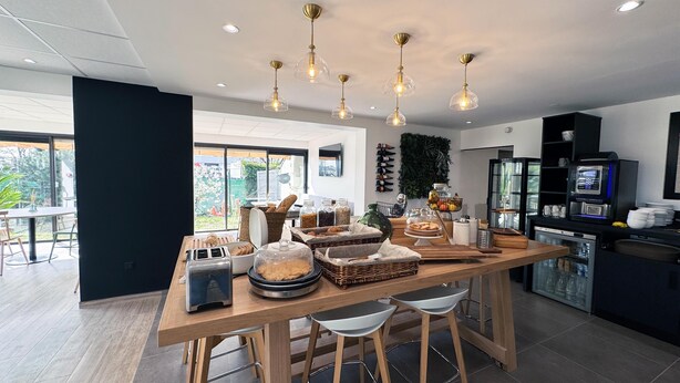 A modern kitchen with a central island, bar stools, a coffee machine, and a view of the outdoors. - Campanile Chambray Les Tours (Chambray-les-Tours)