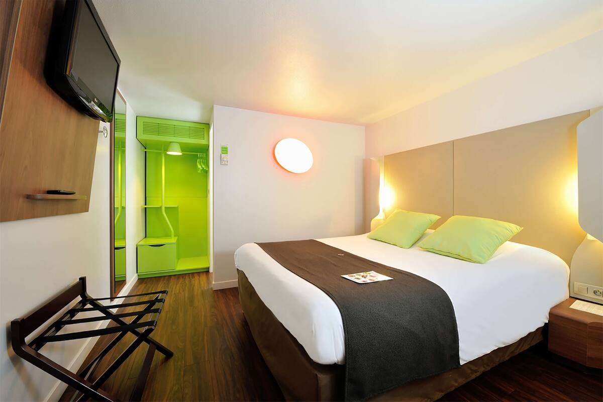 A hotel room with a bed, bedside table, lamp, and a television mounted on the wall.